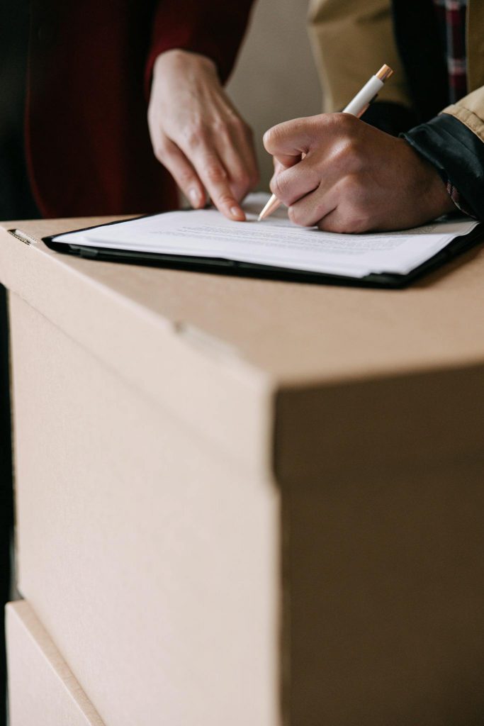 Hands signing lease documents on a cardboard box in an apartment.