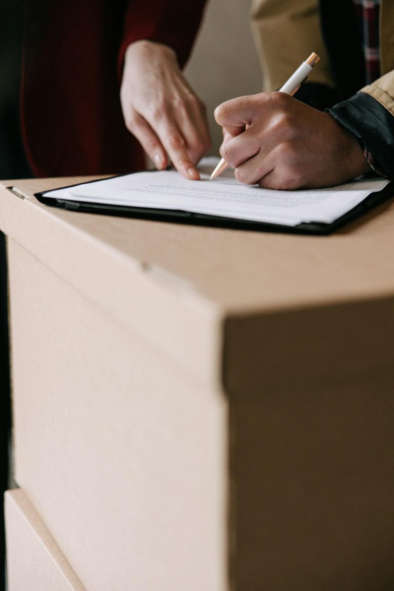 Hands signing lease documents on a cardboard box in an apartment.